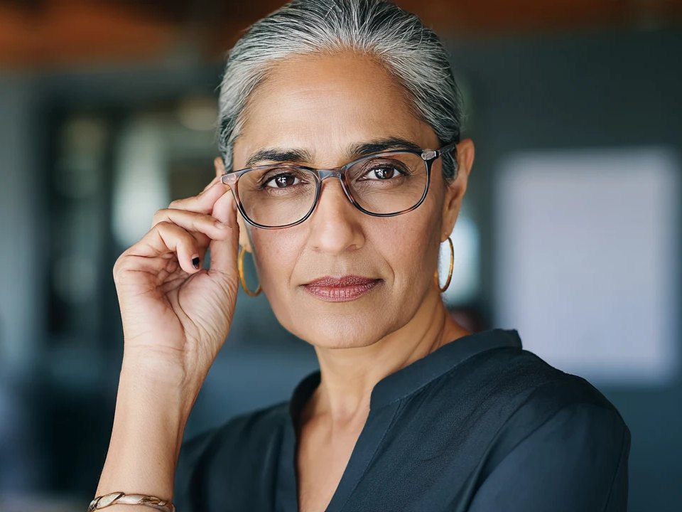 A senior HR leader adjusts her glasses and listens, in a busy open-plan office